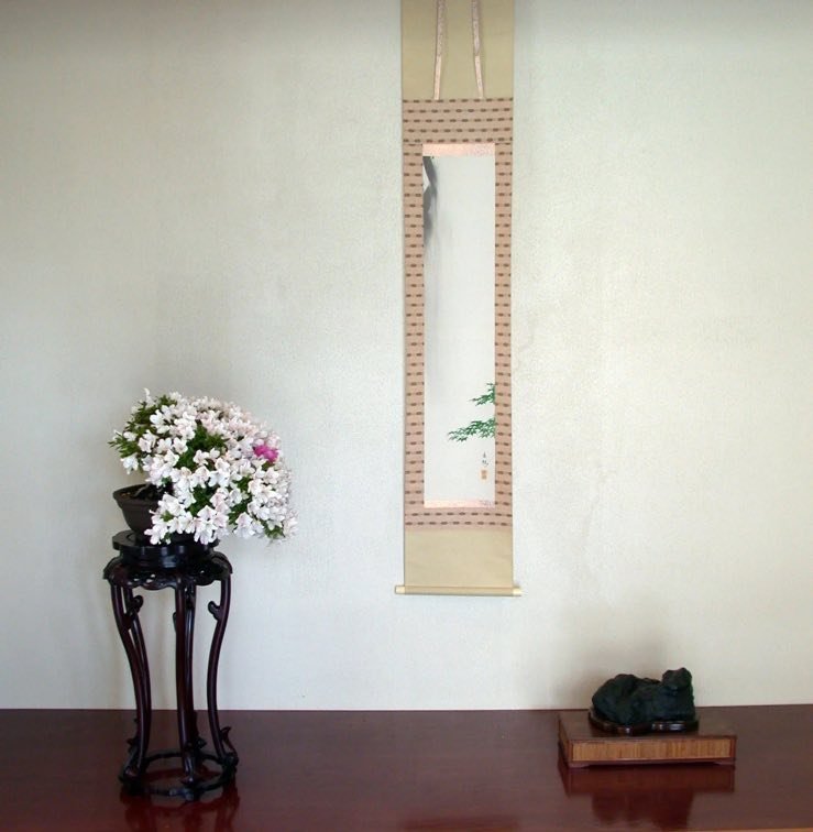 A traditional Japanese hanging scroll displayed beside a flowering accent plant.